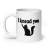 White ceramic coffee mug that has an image of a silhouette of a cat and the text 'I knead you' printed on both sides of the mug.