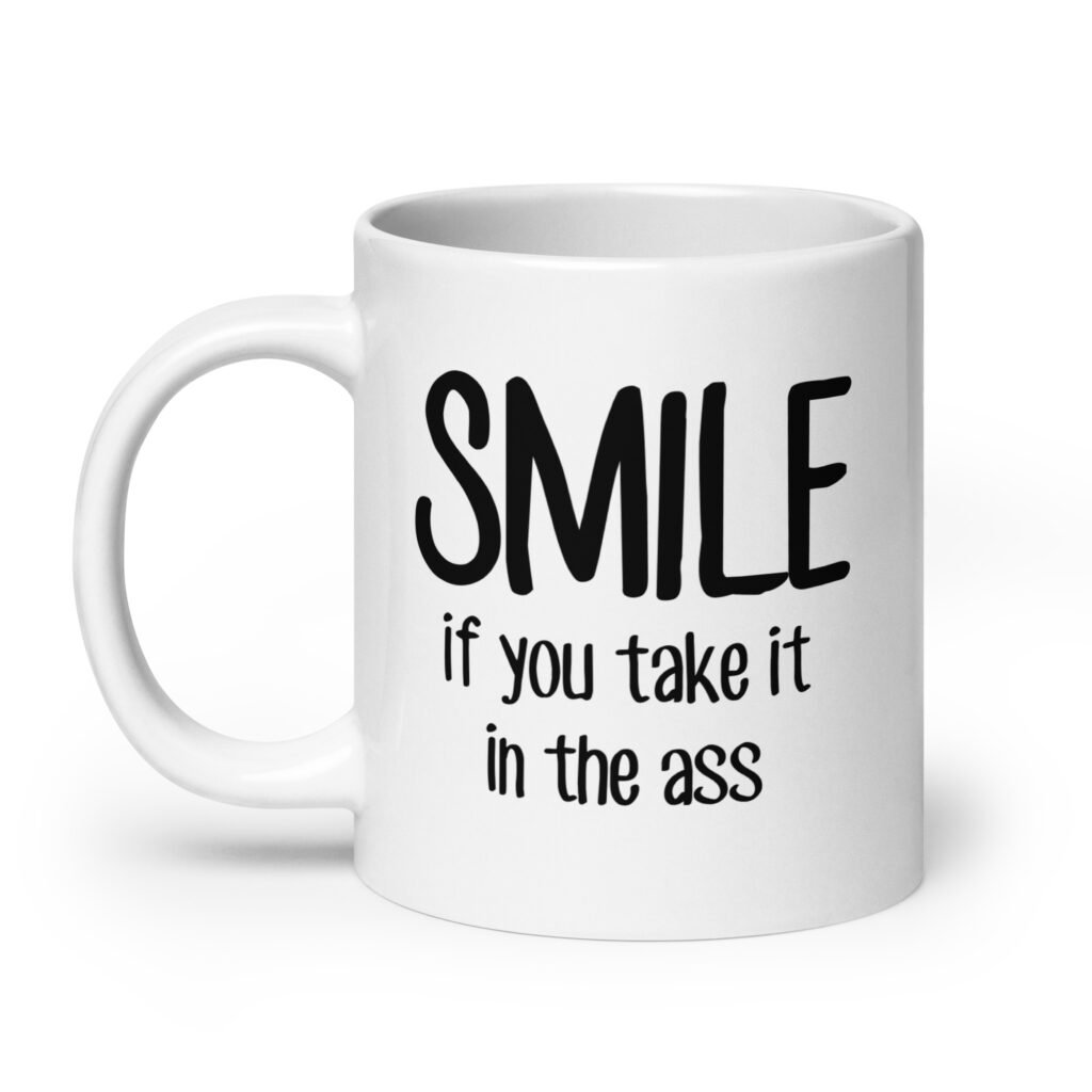 White ceramic mug with the text 'Smile if you take it in the ass' printed on both sides. The word 'smile' is large and the words 'take it in the ass' are much smaller.