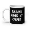 White and black ceramic coffee mug with the text 'Bukkake ruined my carpet' printed in drippy font on both sides.