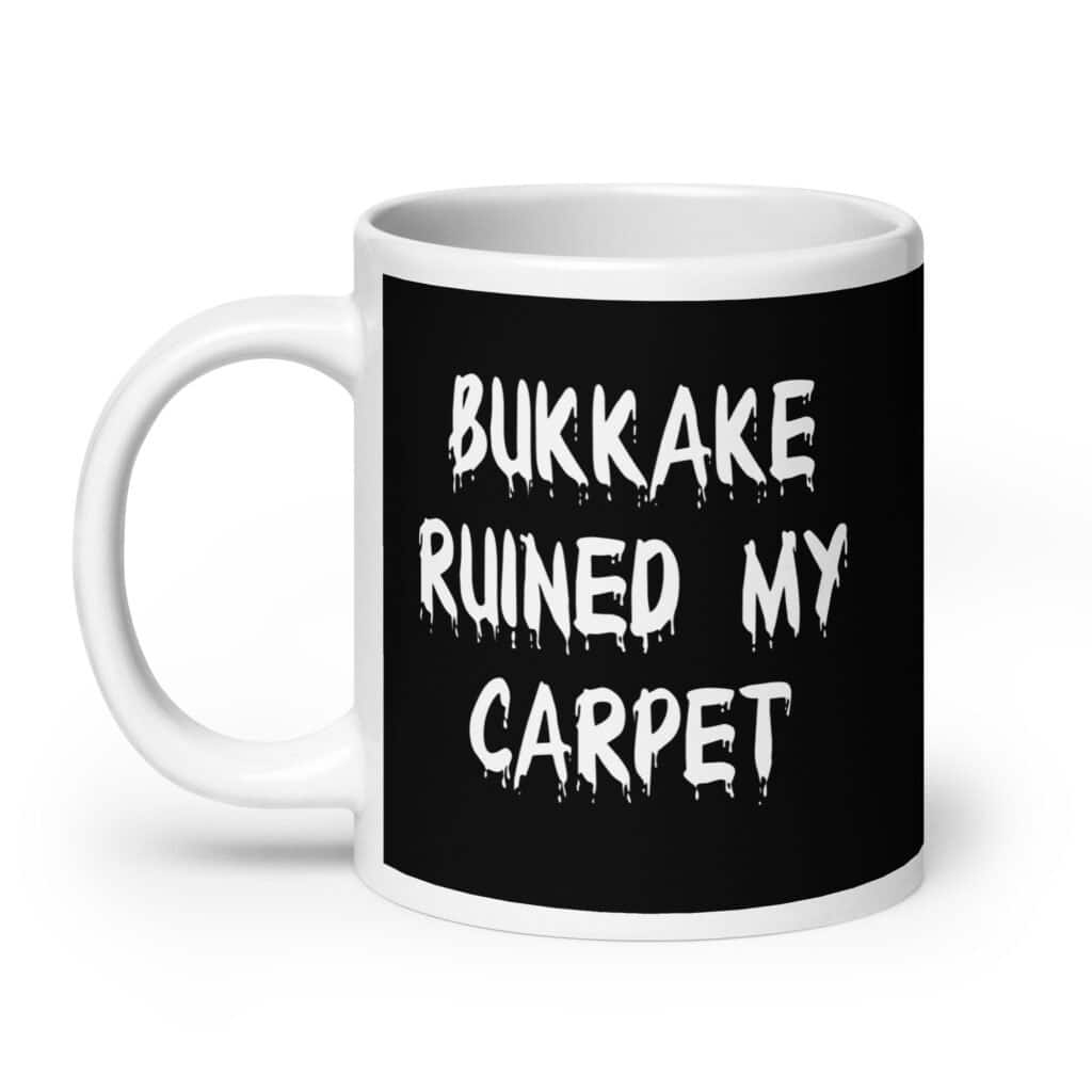 White and black ceramic coffee mug with the text 'Bukkake ruined my carpet' printed in drippy font on both sides.