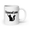 White ceramic coffee mug that has an image of a silhouette of a cat and the text 'I knead you' printed on both sides of the mug.