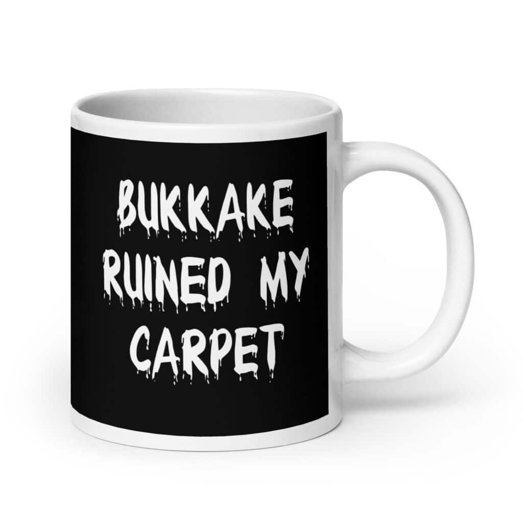 White and black ceramic coffee mug with the text 'Bukkake ruined my carpet' printed in drippy font on both sides.