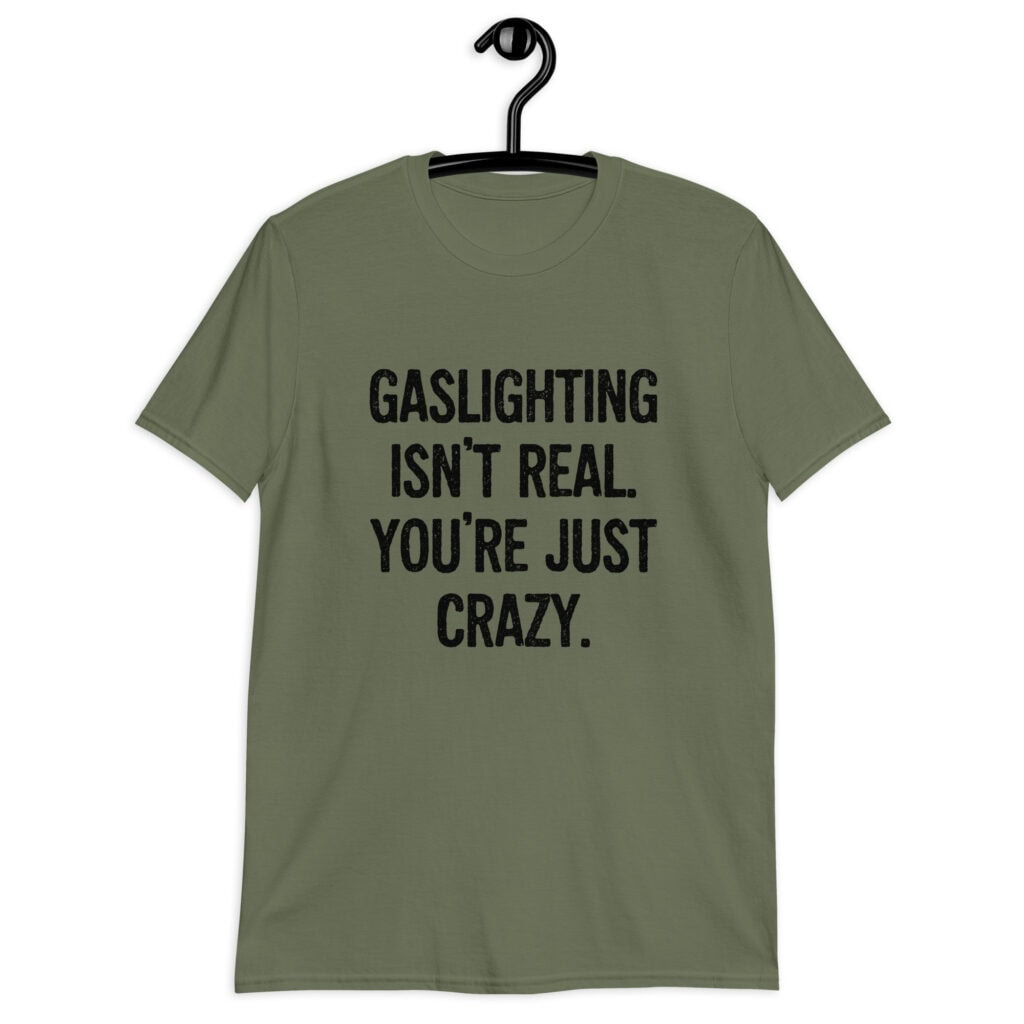 Military green t-shirt with the text 'Gaslighting isn't real. You're just crazy.' printed on the front in bold distressed font.