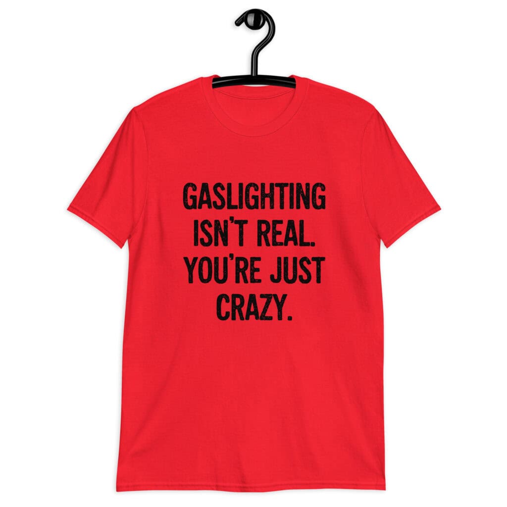 Red t-shirt with the text 'Gaslighting isn't real. You're just crazy.' printed on the front in bold distressed font.