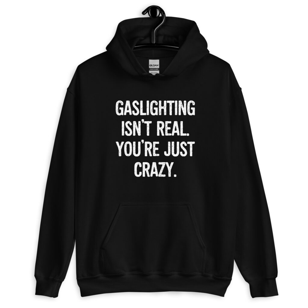Black hoodie sweatshirt with the text 'Gaslighting isn't real. You're just crazy.' printed on the front in bold distressed font.