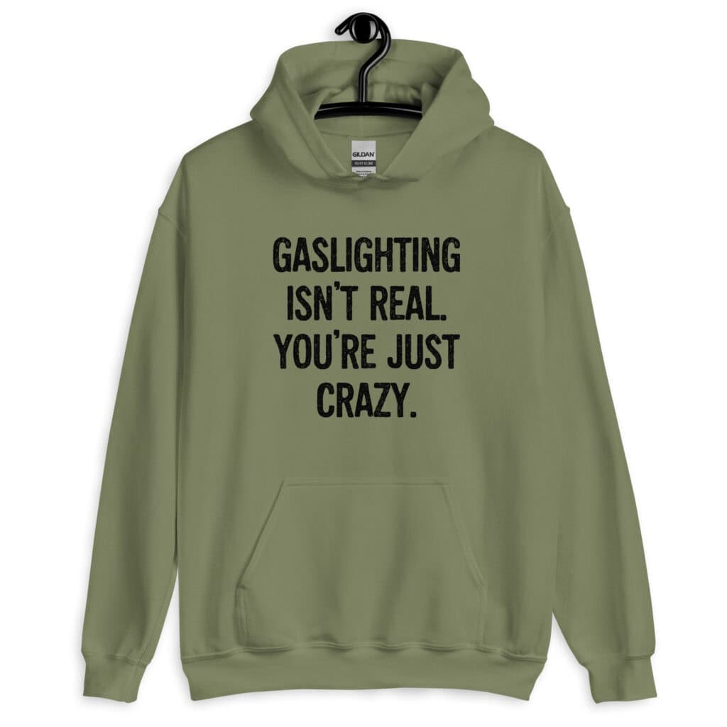 Military green hoodie sweatshirt with the text 'Gaslighting isn't real. You're just crazy.' printed on the front in bold distressed font.