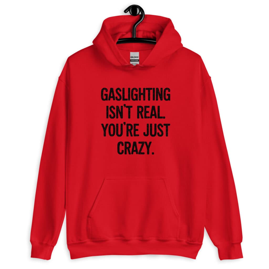 Red hoodie sweatshirt with the text 'Gaslighting isn't real. You're just crazy.' printed on the front in bold distressed font.