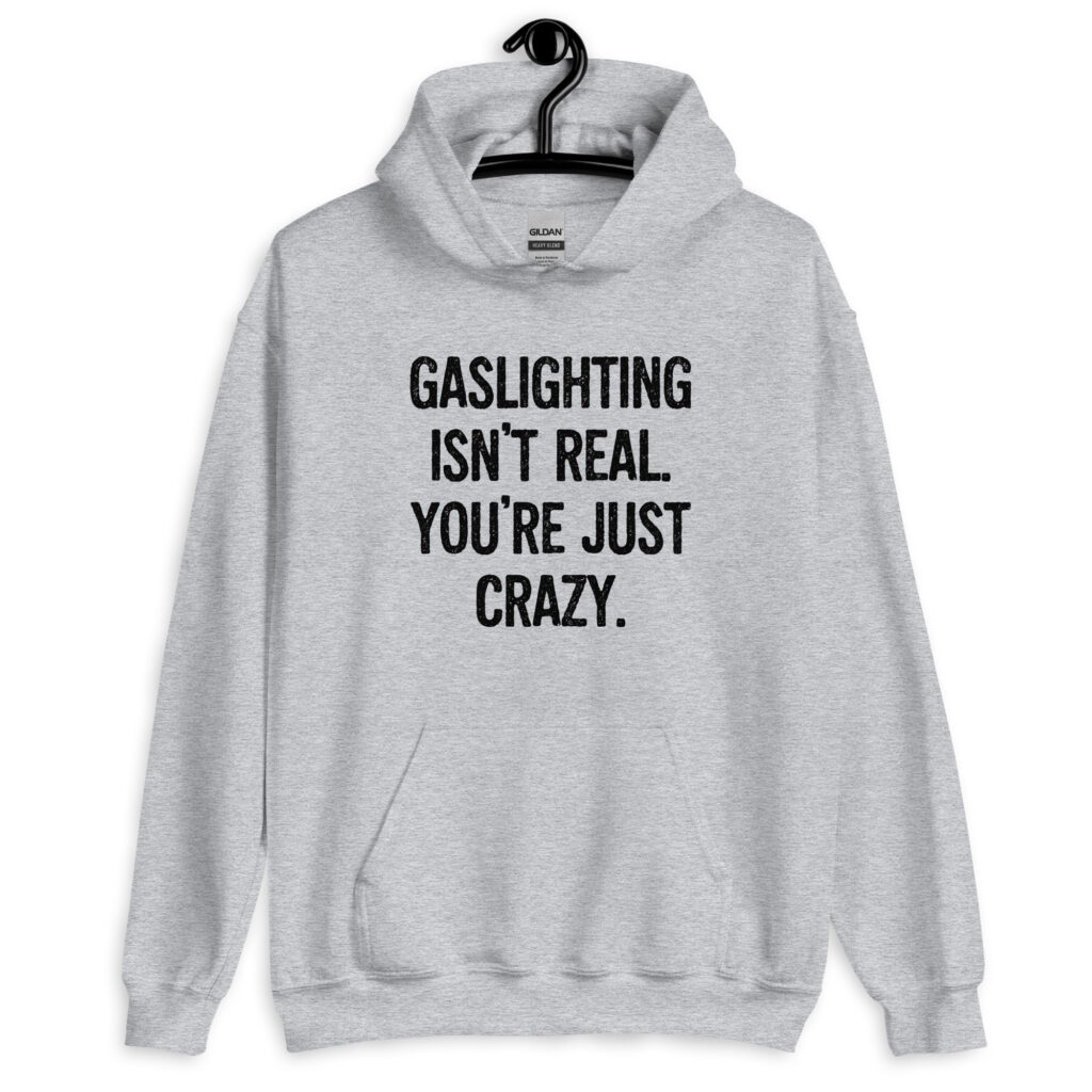 Sport grey hoodie sweatshirt with the text 'Gaslighting isn't real. You're just crazy.' printed on the front in bold distressed font.