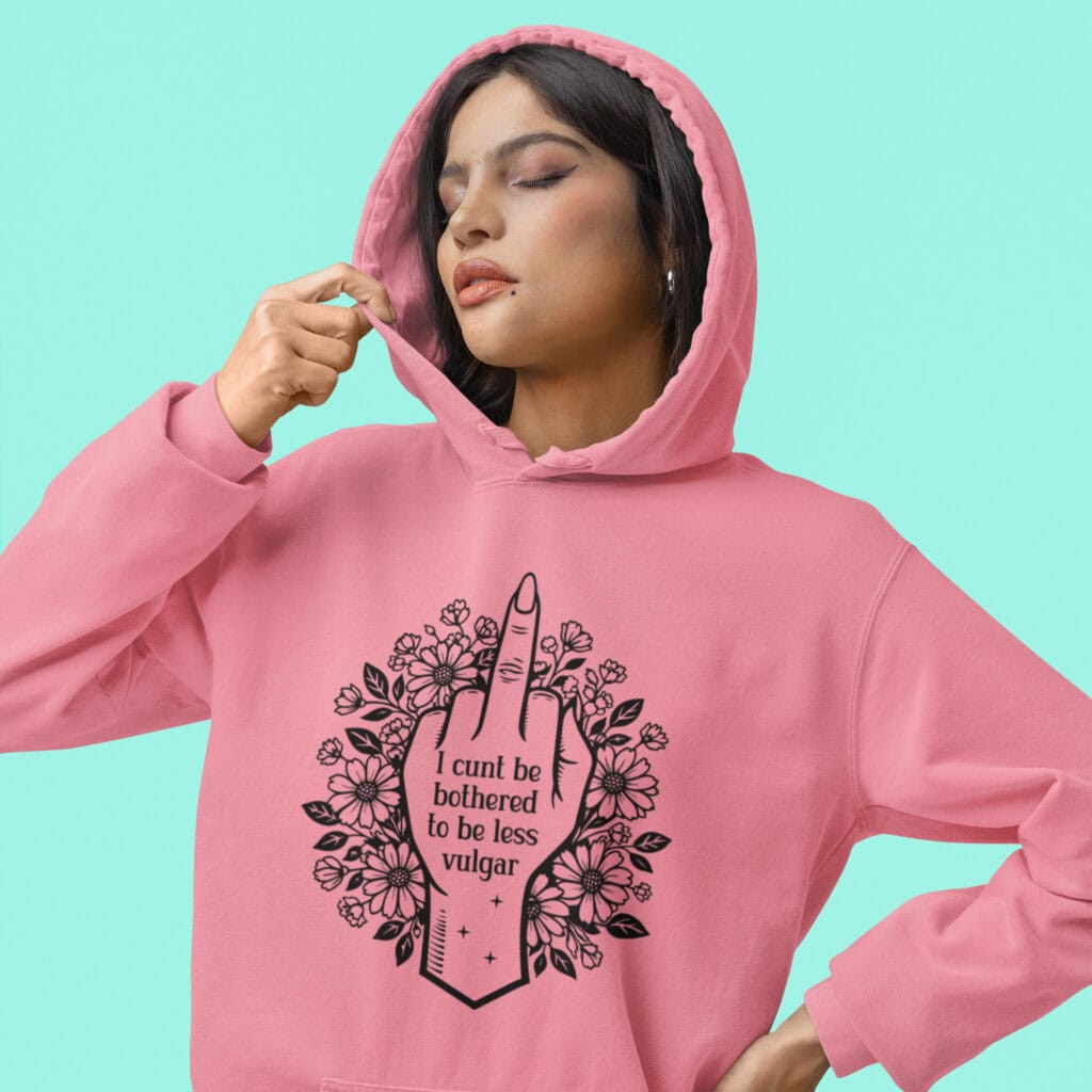 Woman wearing a coral pink color hoodie with a middle finger design on the front and the text 'I cunt be bothered to be less vulgar' printed on the front.