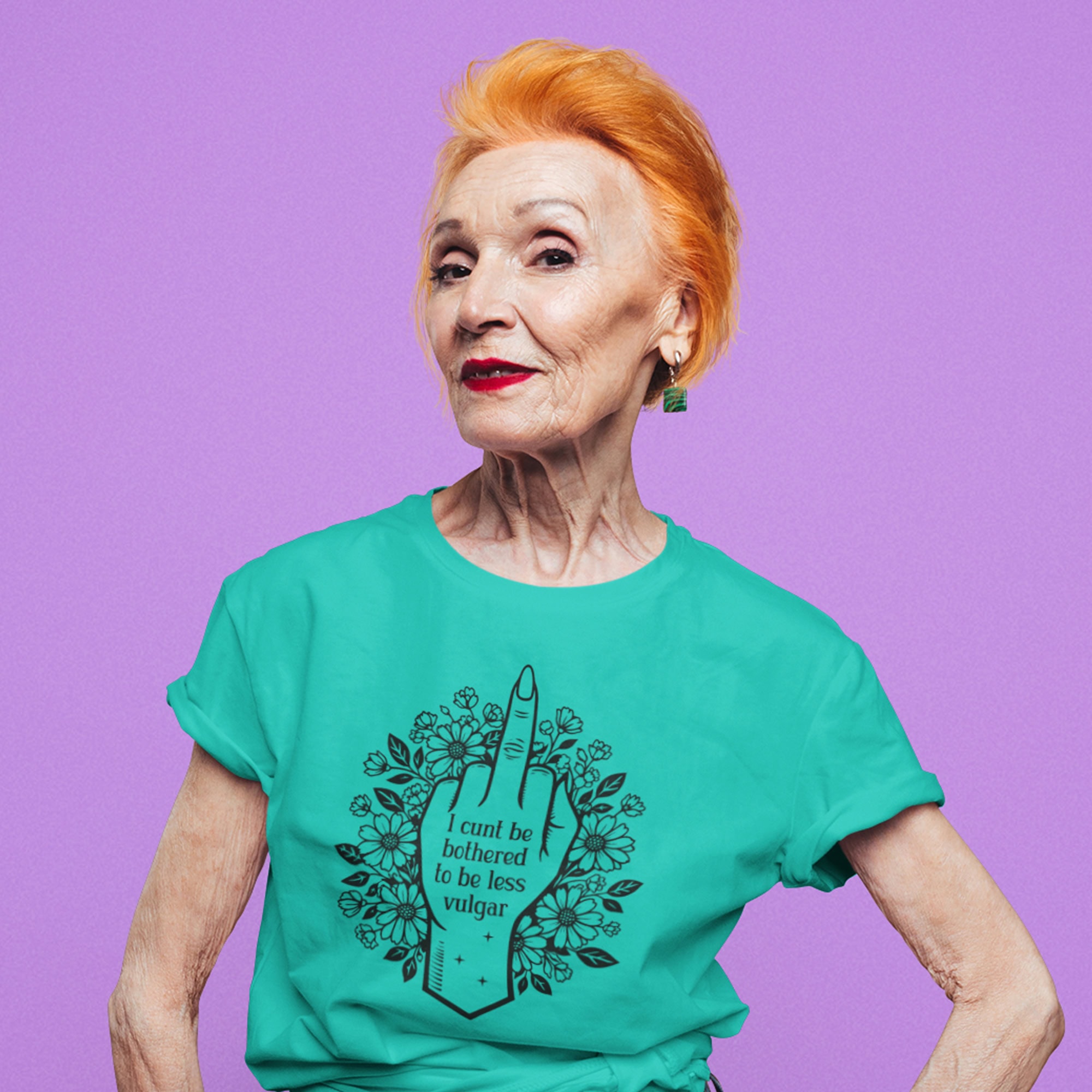 Older red haired woman wearing a jade color t-shirt with a middle finger design on the front and the text 'I cunt be bothered to be less vulgar' printed on the front.