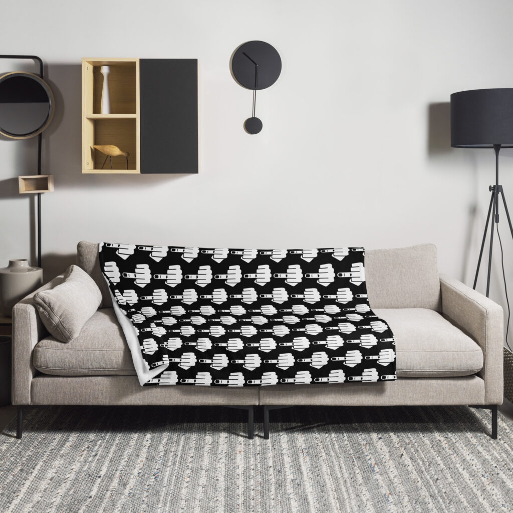 Throw blanket with image of middle finger silhouette printed all over. The blanket is black and the graphic is white. Shown on a sofa.