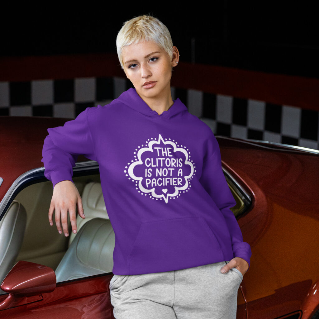 Woman wearing a purple hoodie sweatshirt with the text "The clitoris is not a pacifier" printed on the front.