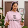 Woman wearing a light pink hoodie sweatshirt with the text 'PEG THE PATRIARCHY' printed on the front.