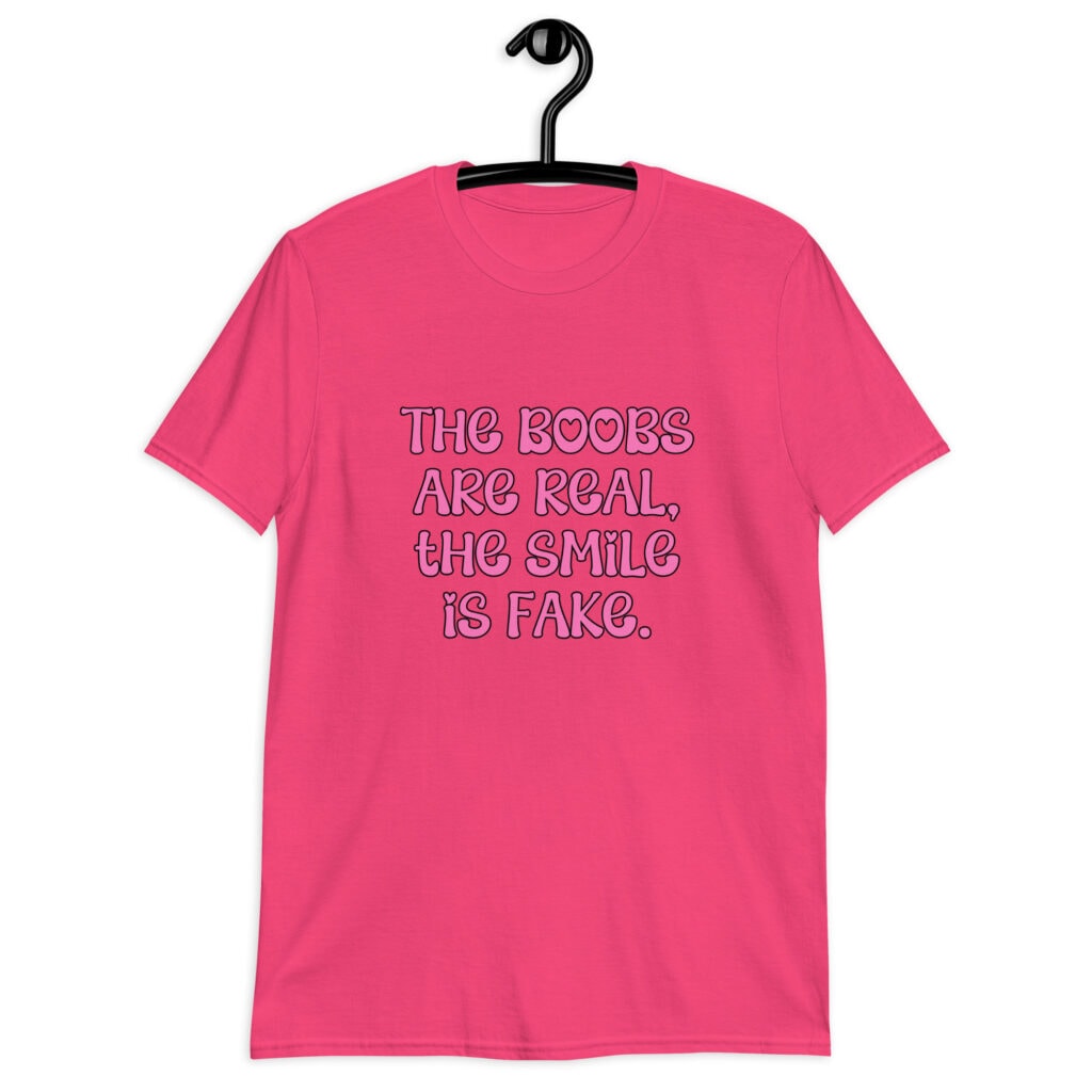 Heliconia pink t-shirt with the text 'The boobs are real, the smile is fake.' printed in pink on the front.