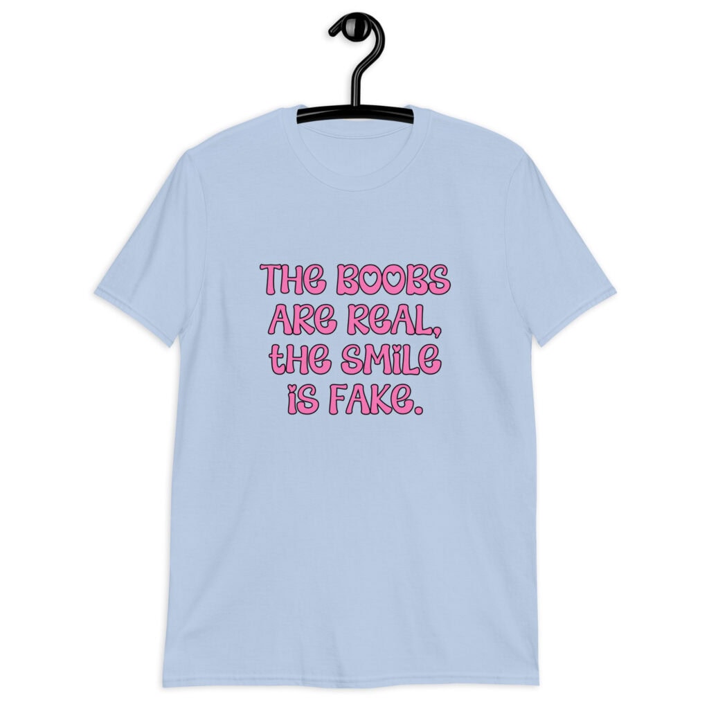 Light blue t-shirt with the text 'The boobs are real, the smile is fake.' printed in pink on the front.