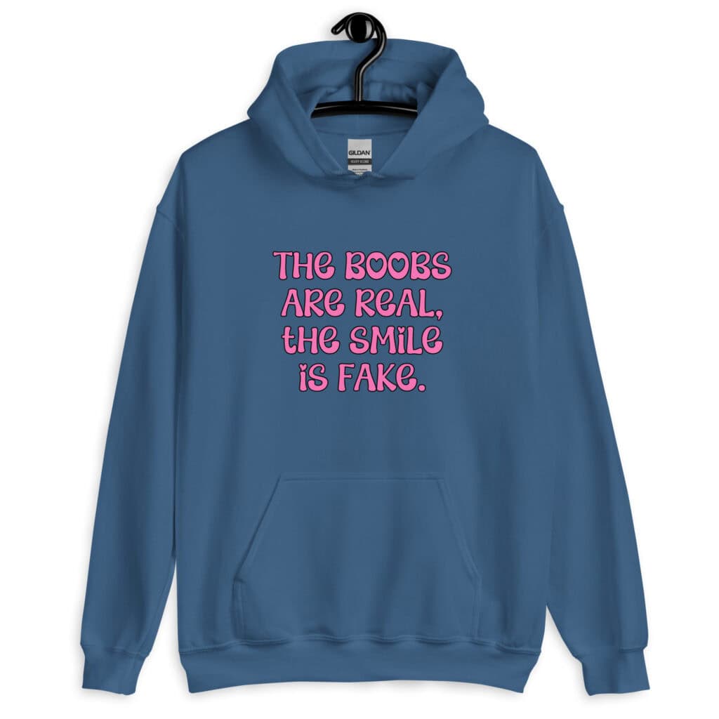 Indigo blue hoodie sweatshirt with the text 'The boobs are real, the smile is fake.' printed in pink on the front.