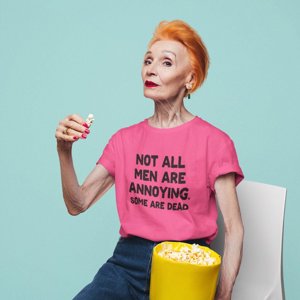Older bold woman wearing a heliconia pink t-shirt with the text 'Not all men are annoying. Some are dead' printed on the front.