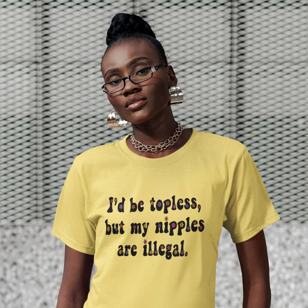 Woman wearing a cornsilk yellow t-shirt with the text 'I'd be topless, but my nipples are illegal.' printed on the front in a floral font.