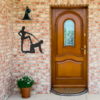 Front porch with brick wall, wooden door, and black steel wall art mounted beside an outdoor light fixture.