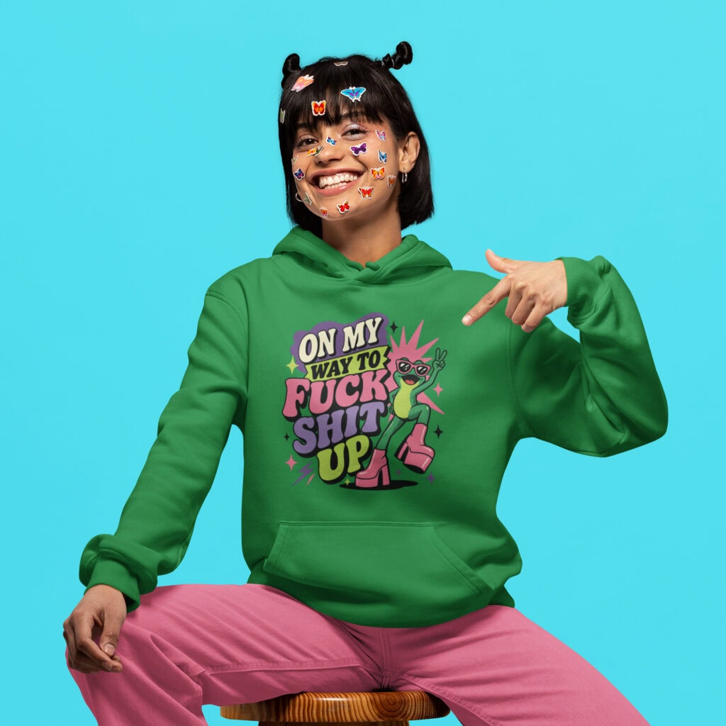 Woman wearing a green hoodie with a retro frog and the phrase “On My Way to Fuck Shit Up” printed on the front.