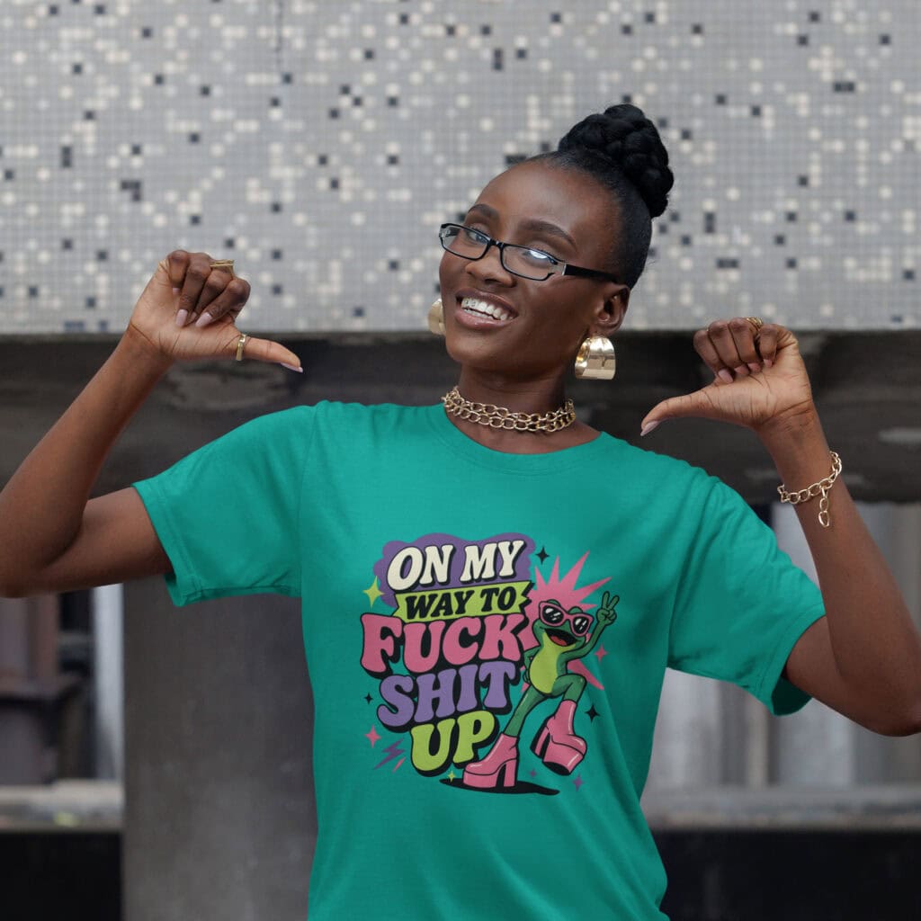 Woman wearing a jade color t-shirt with a retro frog and the phrase “On My Way to Fuck Shit Up” printed on the front.