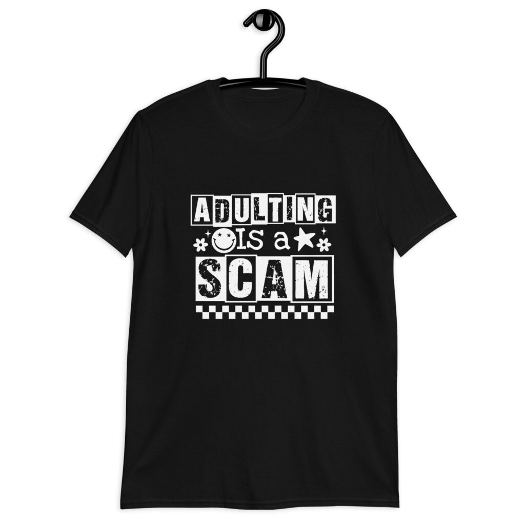 Black t-shirt with bold white text reading ‘Adulting is a Scam’ in mixed block and distressed fonts. The design includes a smiley face, star, and flower icons, with a checkerboard stripe along the bottom.