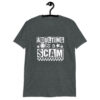 Dark heather grey t-shirt with bold white text reading ‘Adulting is a Scam’ in mixed block and distressed fonts. The design includes a smiley face, star, and flower icons, with a checkerboard stripe along the bottom.