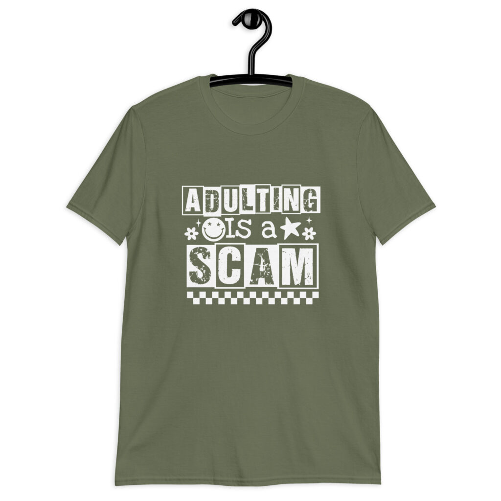 Military green t-shirt with bold white text reading ‘Adulting is a Scam’ in mixed block and distressed fonts. The design includes a smiley face, star, and flower icons, with a checkerboard stripe along the bottom.