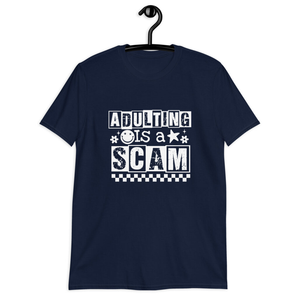 Navy blue t-shirt with bold white text reading ‘Adulting is a Scam’ in mixed block and distressed fonts. The design includes a smiley face, star, and flower icons, with a checkerboard stripe along the bottom.