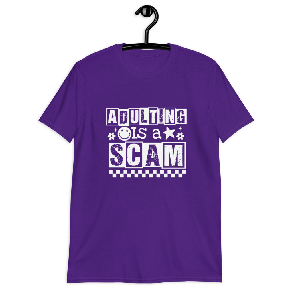 Purple t-shirt with bold white text reading ‘Adulting is a Scam’ in mixed block and distressed fonts. The design includes a smiley face, star, and flower icons, with a checkerboard stripe along the bottom.