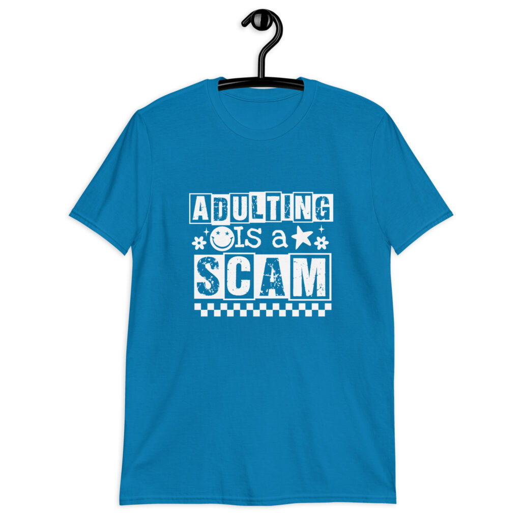 Sapphire blue t-shirt with bold white text reading ‘Adulting is a Scam’ in mixed block and distressed fonts. The design includes a smiley face, star, and flower icons, with a checkerboard stripe along the bottom.