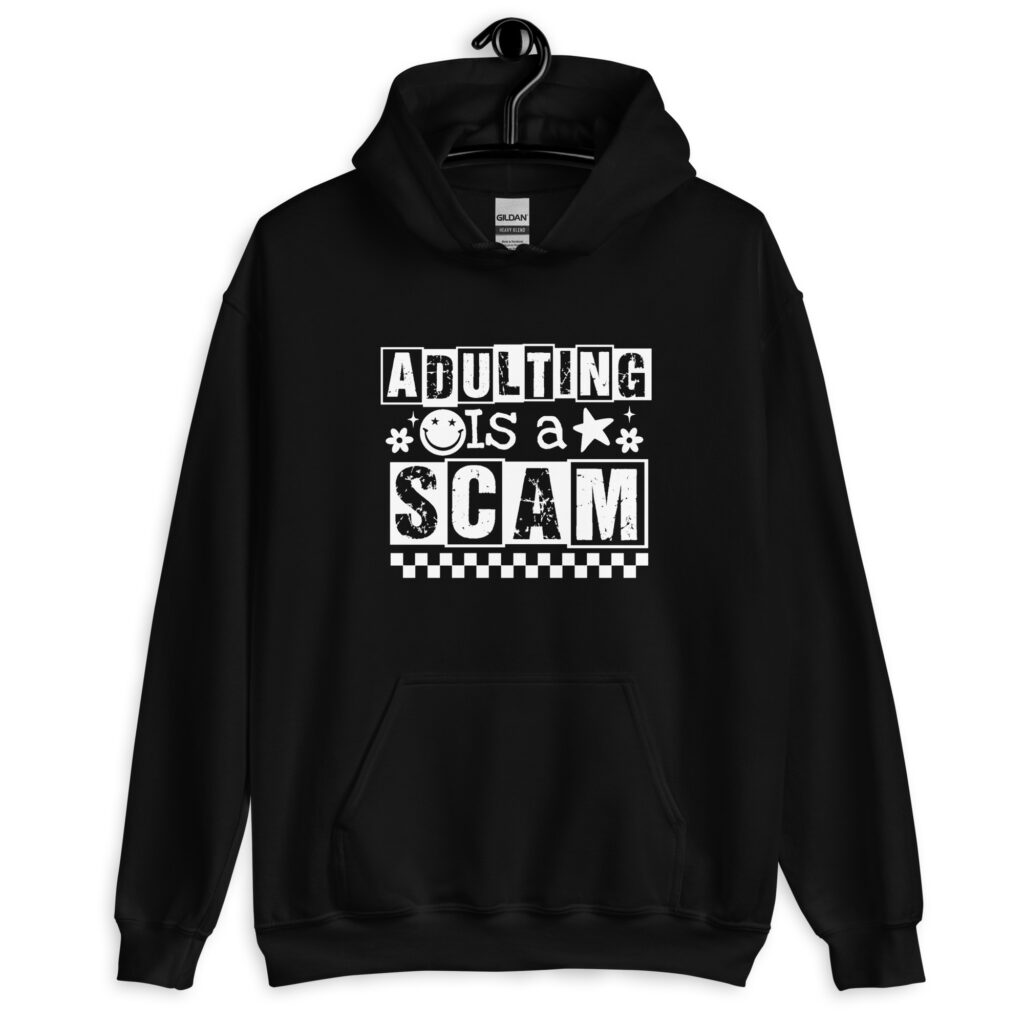 Black hoodie sweatshirt with bold white text reading ‘Adulting is a Scam’ in mixed block and distressed fonts. The design includes a smiley face, star, and flower icons, with a checkerboard stripe along the bottom.