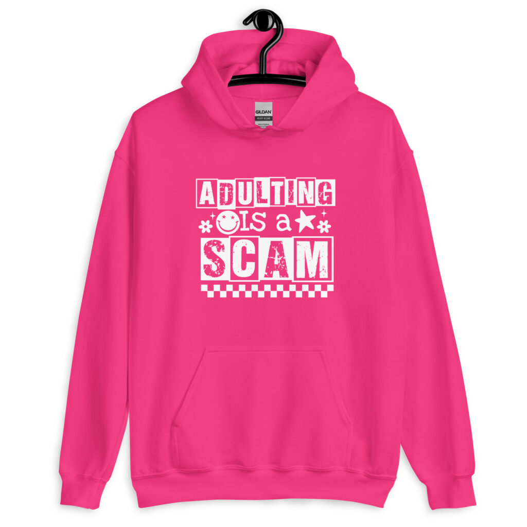 Heliconia pink hoodie sweatshirt with bold white text reading ‘Adulting is a Scam’ in mixed block and distressed fonts. The design includes a smiley face, star, and flower icons, with a checkerboard stripe along the bottom.
