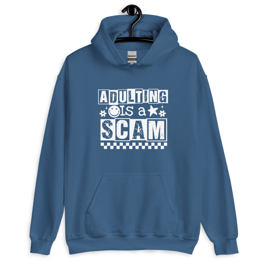 Indigo blue hoodie sweatshirt with bold white text reading ‘Adulting is a Scam’ in mixed block and distressed fonts. The design includes a smiley face, star, and flower icons, with a checkerboard stripe along the bottom.