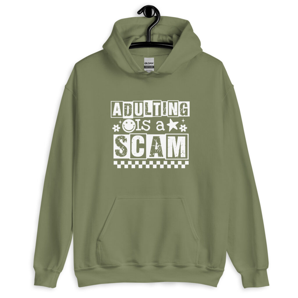 Military green hoodie with bold white text reading ‘Adulting is a Scam’ in mixed block and distressed fonts. The design includes a smiley face, star, and flower icons, with a checkerboard stripe along the bottom.
