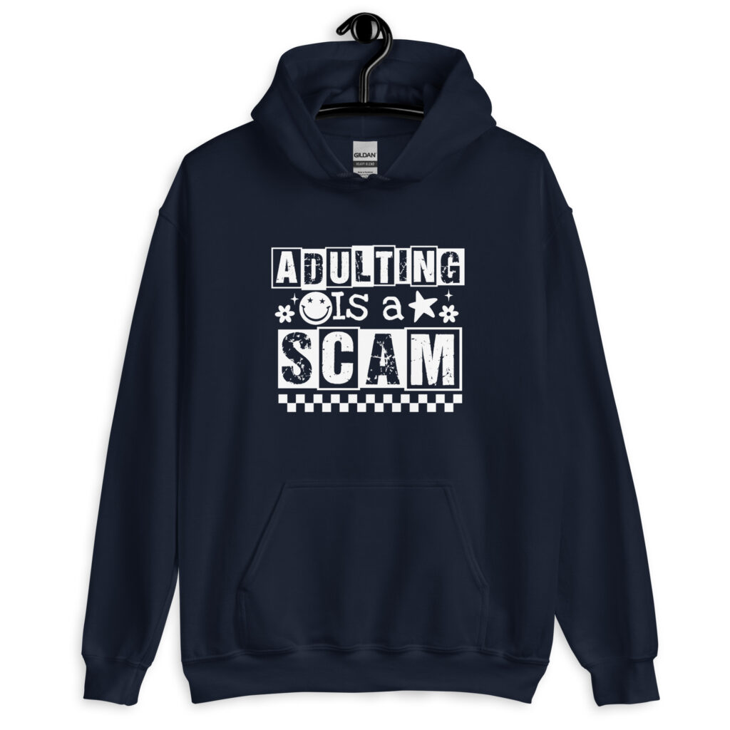 Navy blue hoodie sweatshirt with bold white text reading ‘Adulting is a Scam’ in mixed block and distressed fonts. The design includes a smiley face, star, and flower icons, with a checkerboard stripe along the bottom.