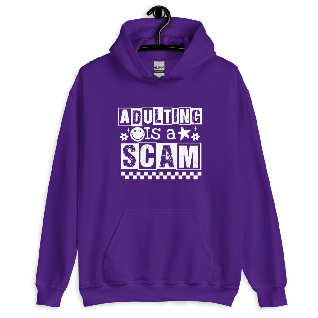 Purple hoodie sweatshirt with bold white text reading ‘Adulting is a Scam’ in mixed block and distressed fonts. The design includes a smiley face, star, and flower icons, with a checkerboard stripe along the bottom.