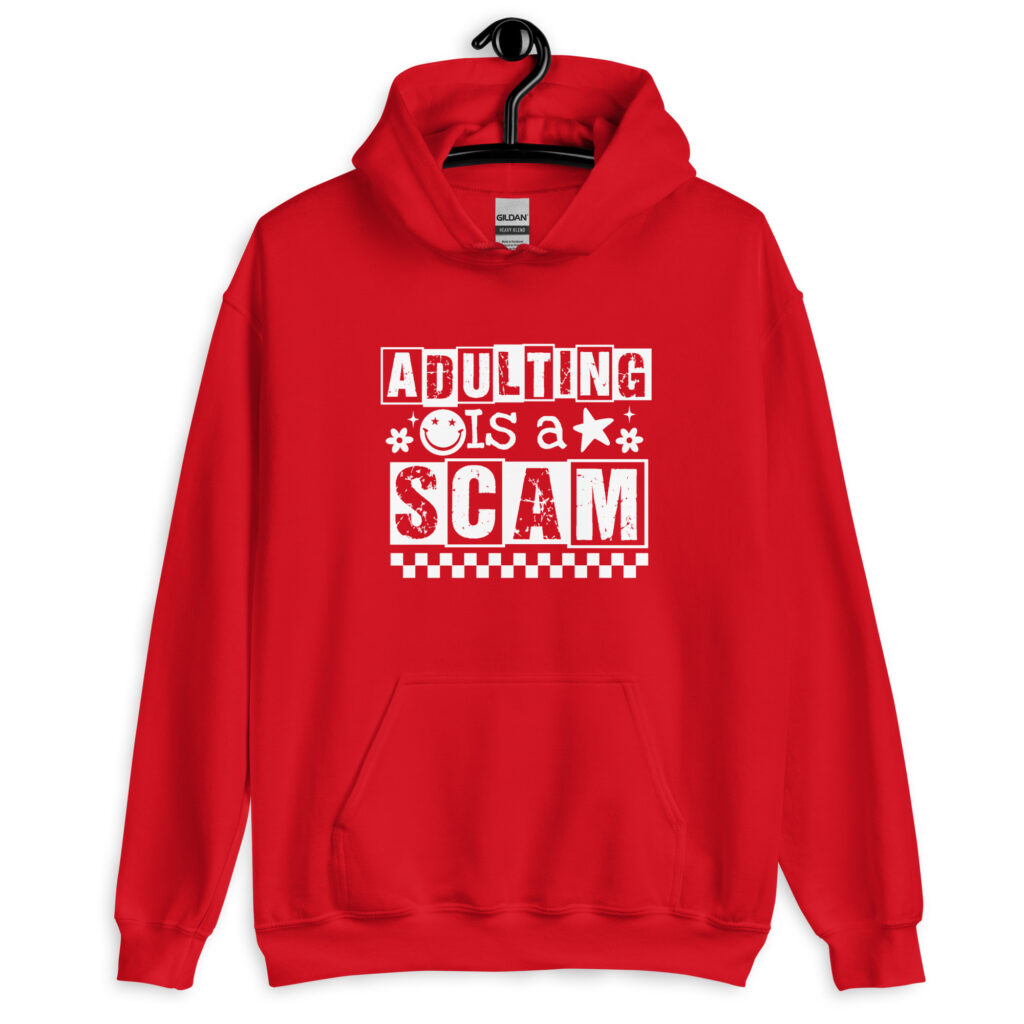 Red hoodie sweatshirt with bold white text reading ‘Adulting is a Scam’ in mixed block and distressed fonts. The design includes a smiley face, star, and flower icons, with a checkerboard stripe along the bottom.