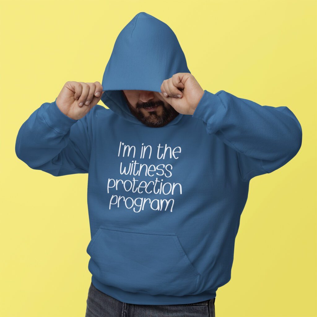 Man wearing an indigo blue hoodie sweatshirt with the text 'I'm in the witness protection program' printed on the front.