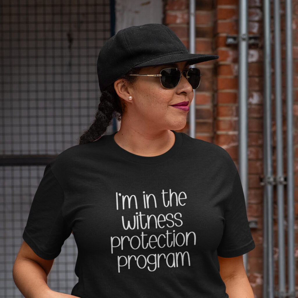 Woman wearing a black t-shirt with the text 'I'm in the witness protection program' printed on the front.